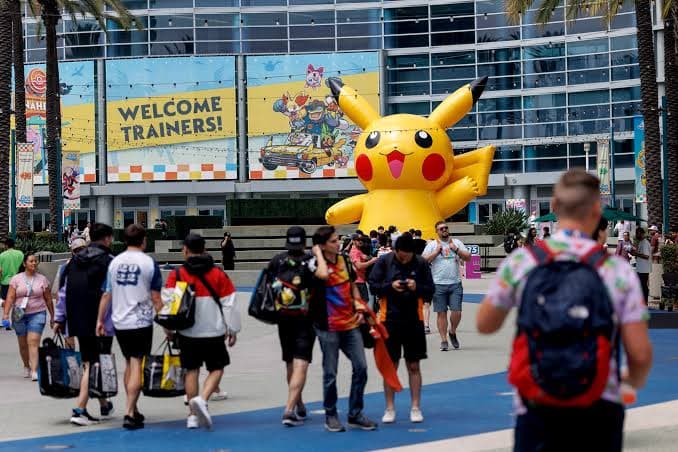 A large inflatable Pikachu balloon and Welcome Trainers signage outside a convention center entrance, attendees walking past