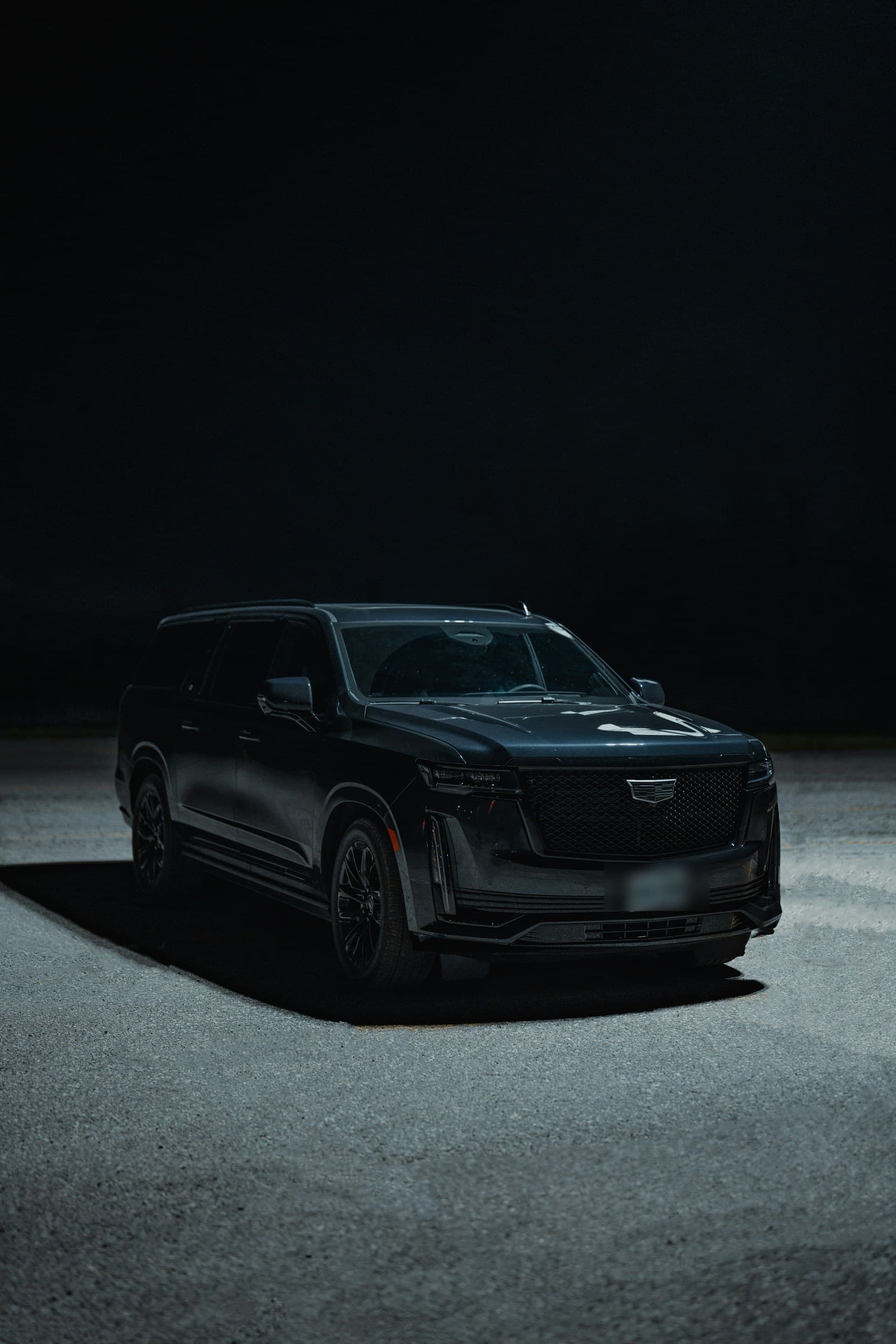 A dark extended length luxury SUV lit dramatically at night
