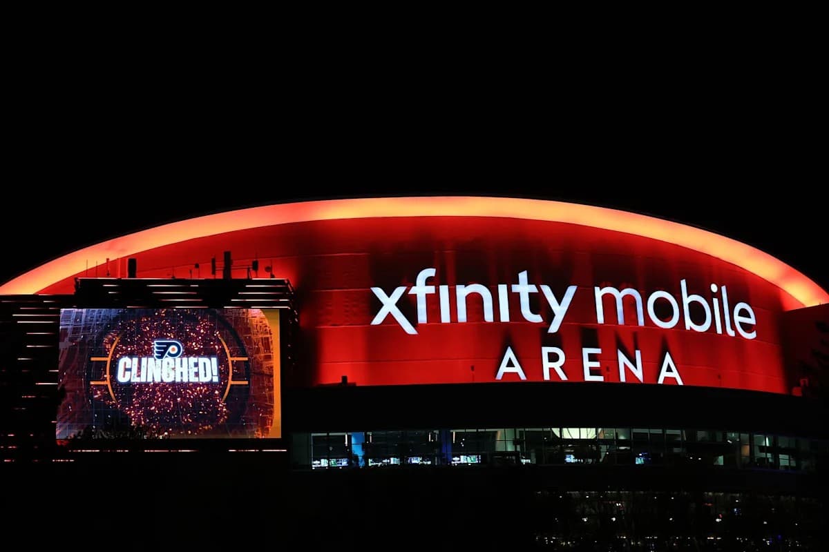 The illuminated exterior of a downtown Philadelphia sports arena at night, screens lit above the entrance