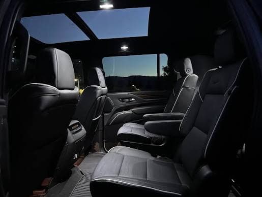 The rear captain's chairs of a Cadillac Escalade at night, sunroof open above