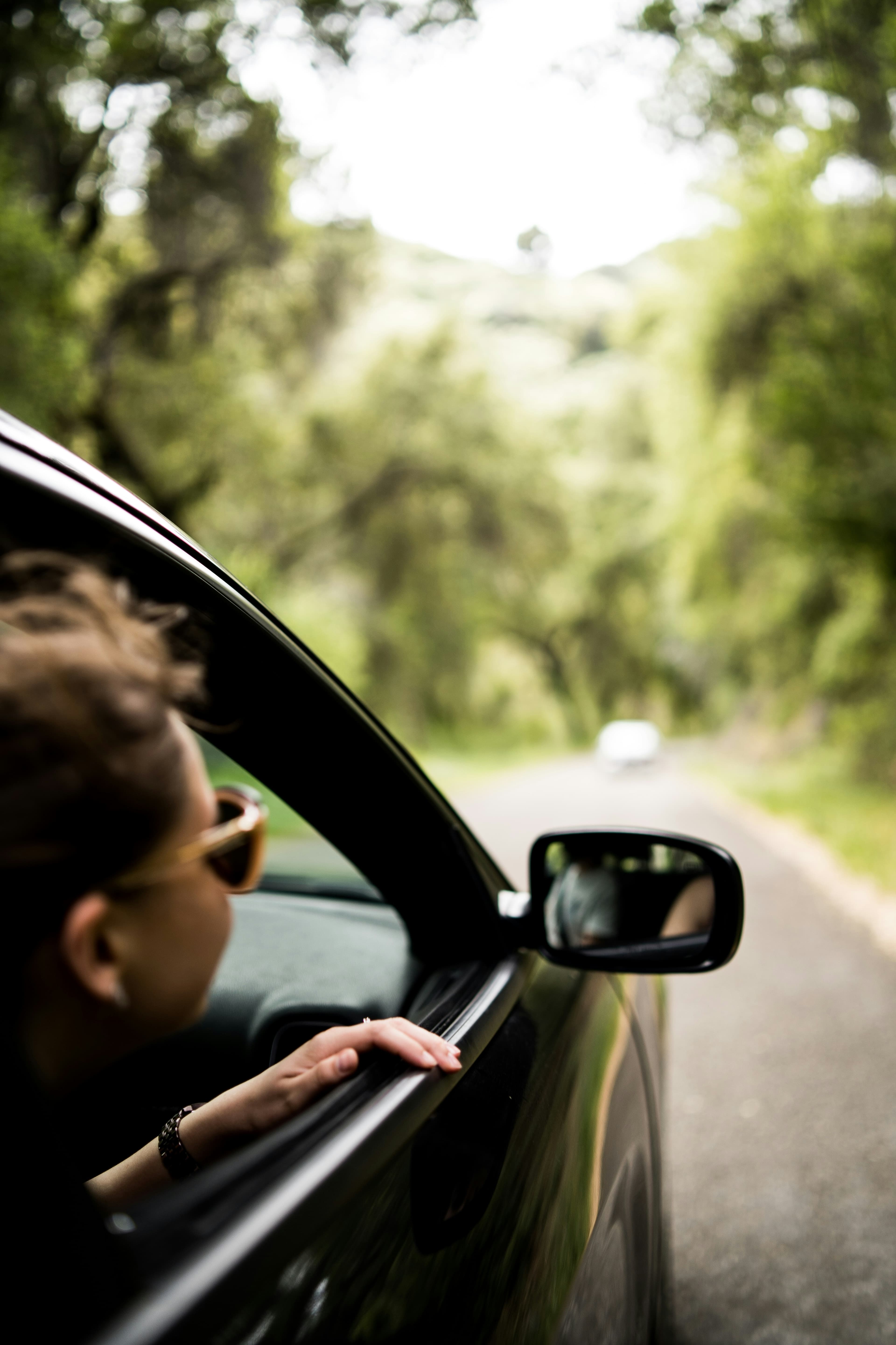 A traveller resting a hand out of an open car window on a tree-lined road