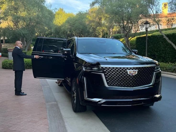 A black Cadillac Escalade parked at a tree lined driveway entrance