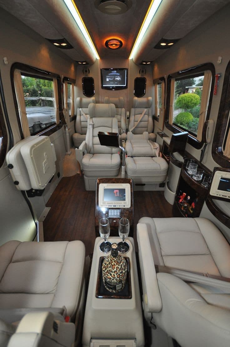 The rear cabin of a custom Sprinter conversion, facing captain's chairs and a wood console
