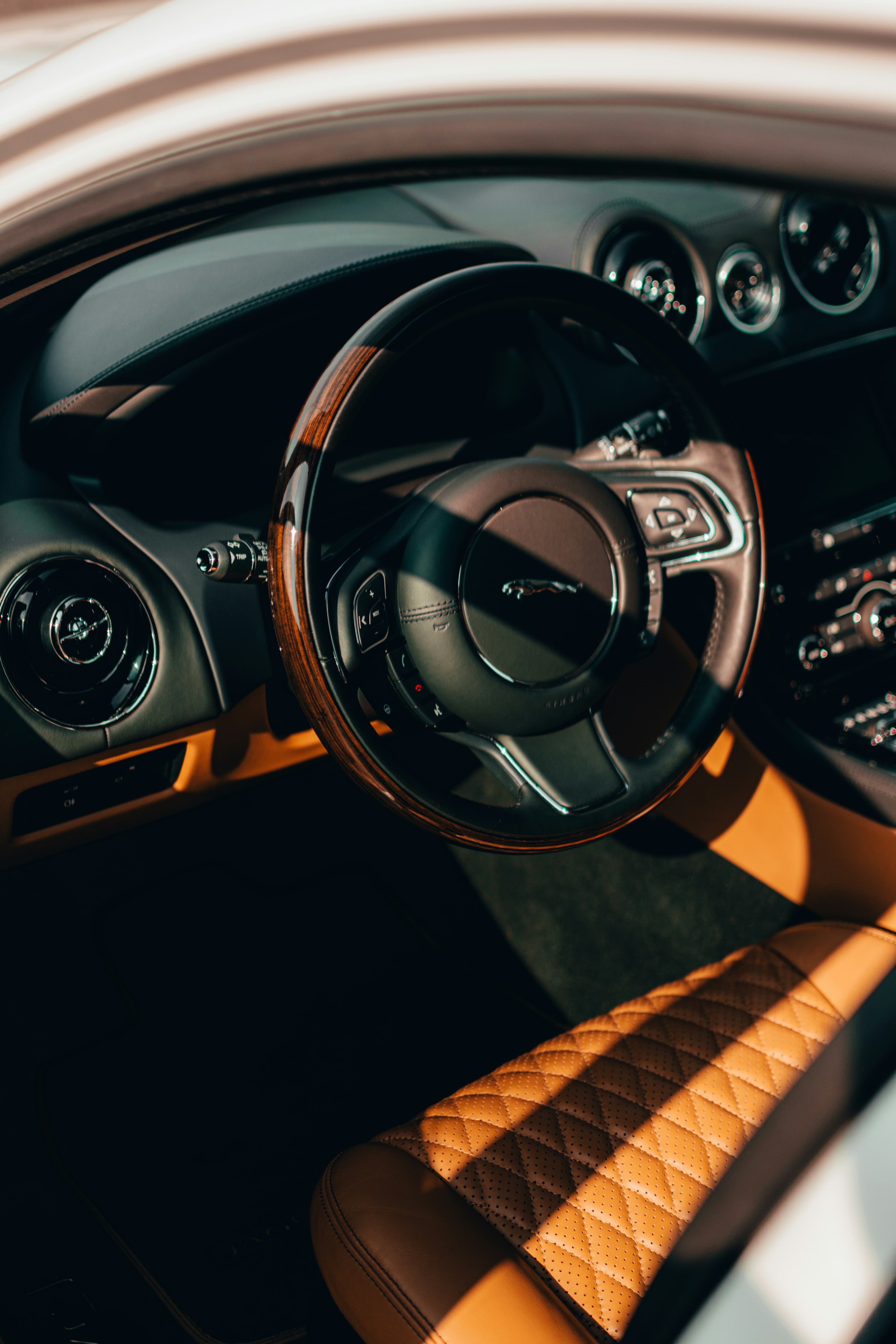 Sunlight across a hand-finished steering wheel and tan leather car interior