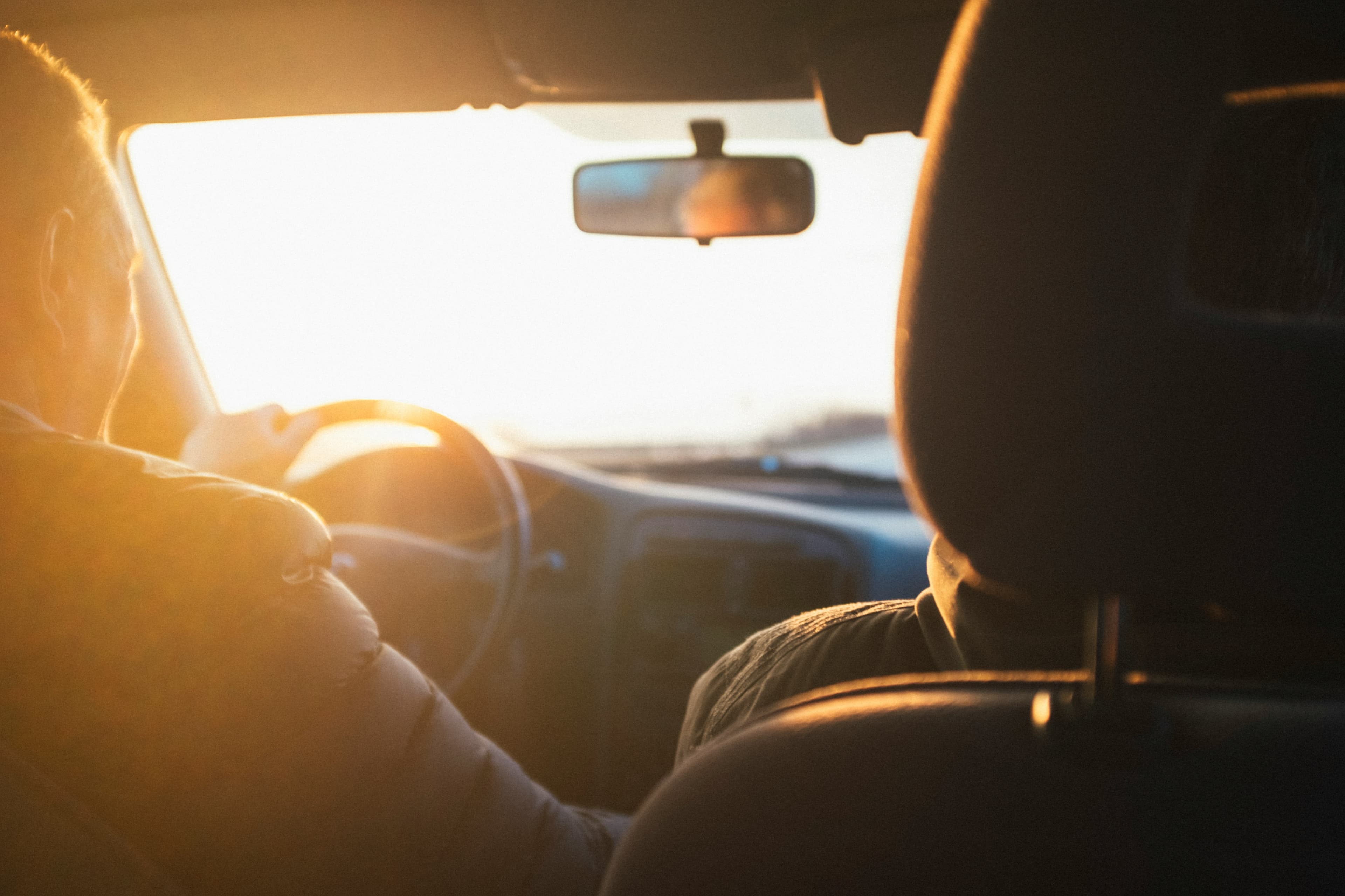 A driver setting off at sunset, warm light filling the car