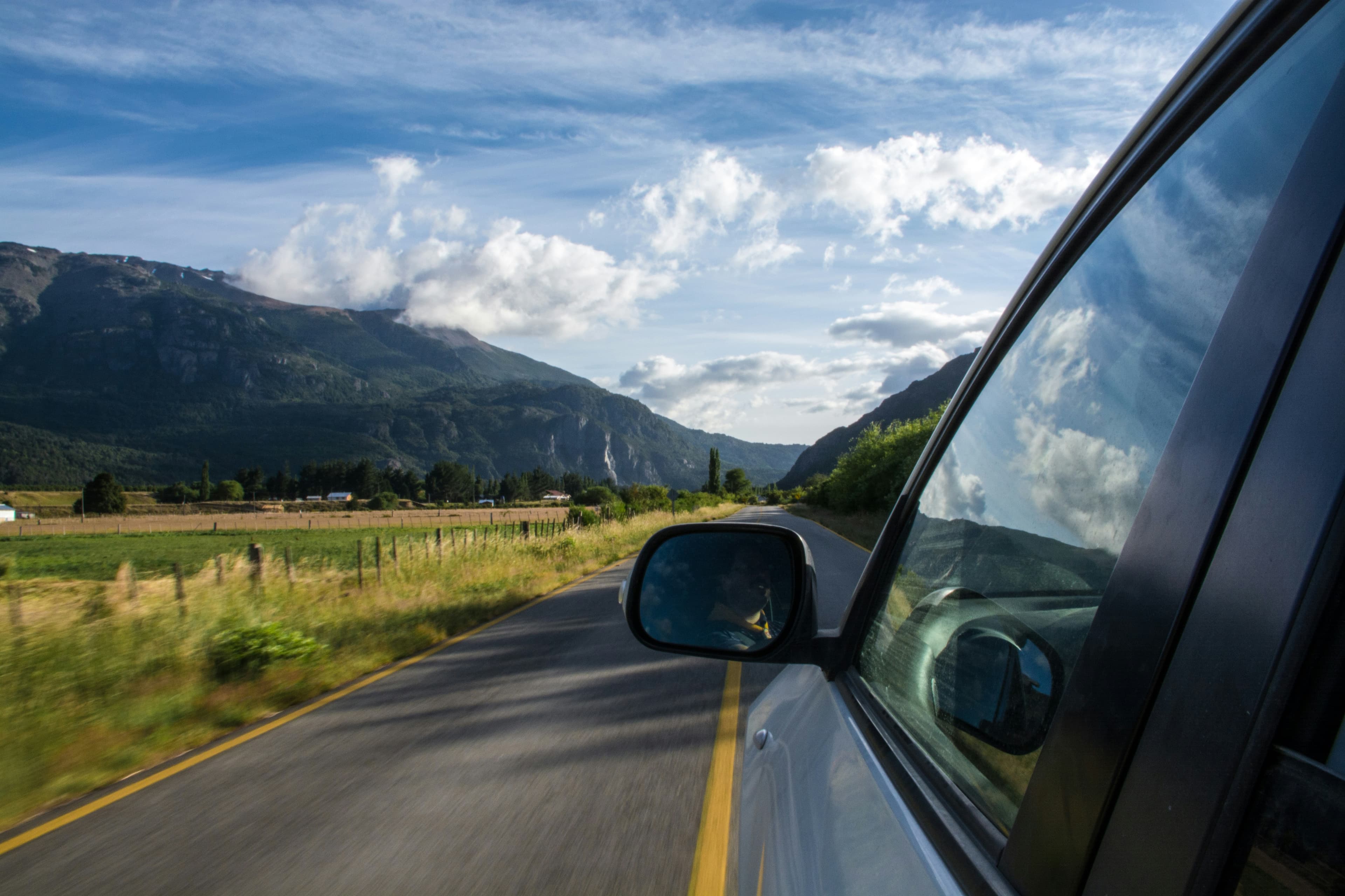 A side mirror reflecting a mountain valley while driving
