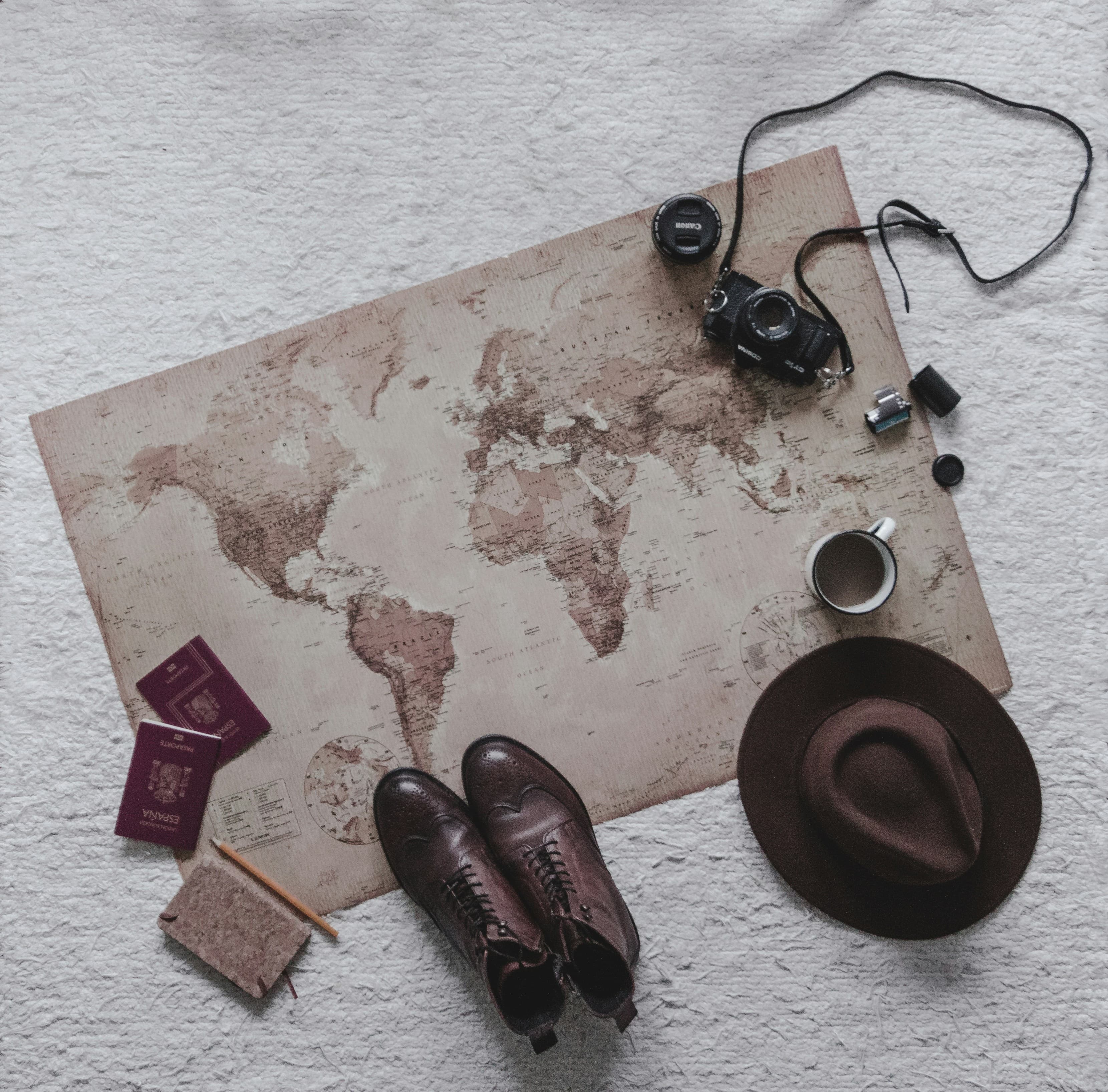 A world map laid out with passports, a camera, a hat and boots while a route is planned